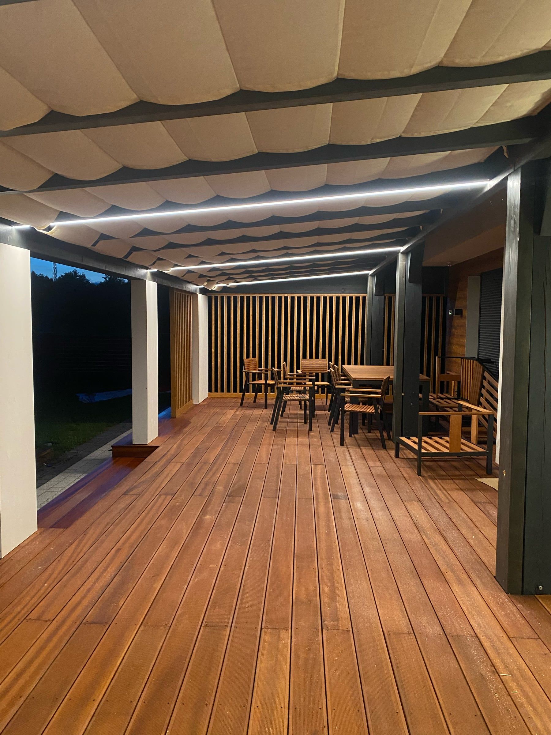 Taras pod pergolą z drewnianą podłogą oświetlony liniami LED wzdłuż belek